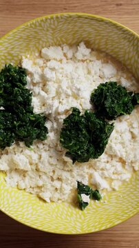 Adding Wilted Spinach To Feta Cheese Bowl Top View Vertical