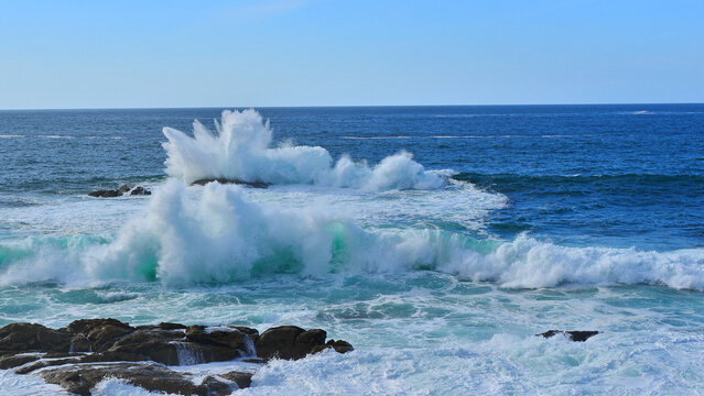 The ocean waves crashing violently against the rocks on a clear day in mid-autumn.
