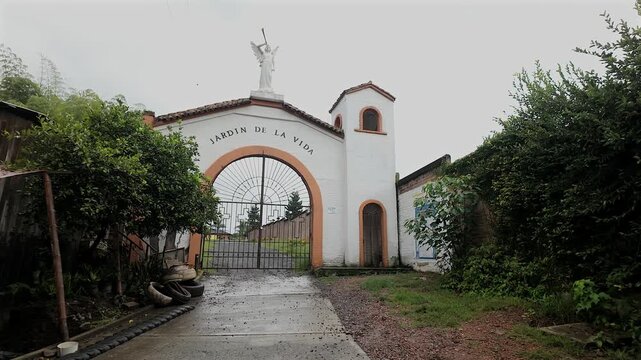 white arched entrance gate to a cemetery named jardin de la vida under a cloudy sky