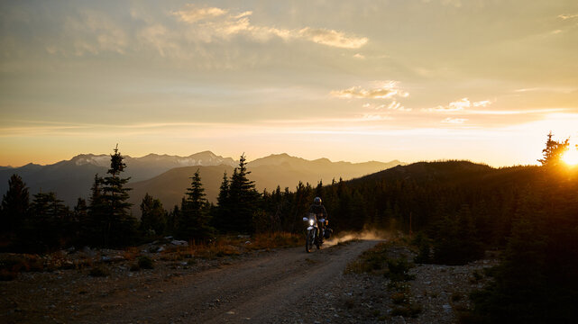 Motorcycle rides on a dirt road during sunset in the mountains