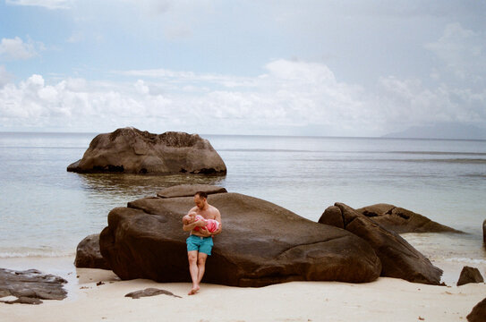 A man and a child are sitting on a large stone by the water.