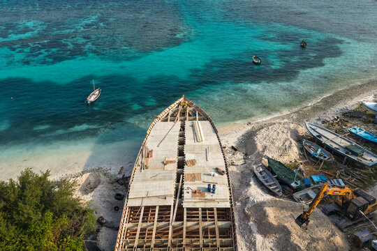 Aerial view of a large wooden boat under construction at the Vaikaradhoo ship yard on a sandy beach by turquoise waters in Vaikaradhoo, Haa Dhaalu City, Maldives.