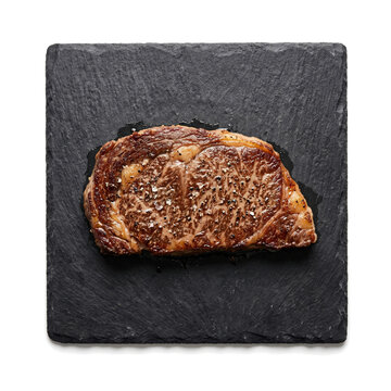 Grilled ribeye steak piece served on dark slate stone board