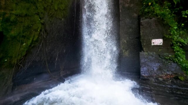 Slow motion shot of Sumampan waterfall in jungle. Location: Ubud, Bali. Camera pans downwards following the water as it hits the pool of water splashing on the rocks. 