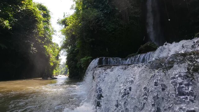 Slow motion shot of powerful streams and cascades of water entering the river in the jungle.  Sumampan waterfall in forest. Location: Ubud, Bali, Indonesia. A sun drenched jungle valley river. 