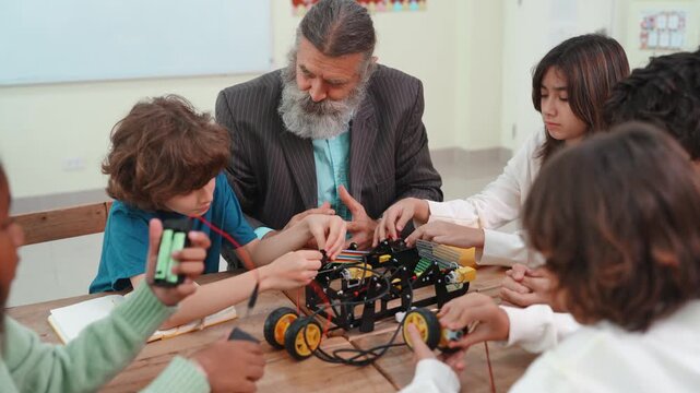 Senior teacher and diverse students building robot in STEM class. Children learning science and engineering project together in elementary school classroom.
