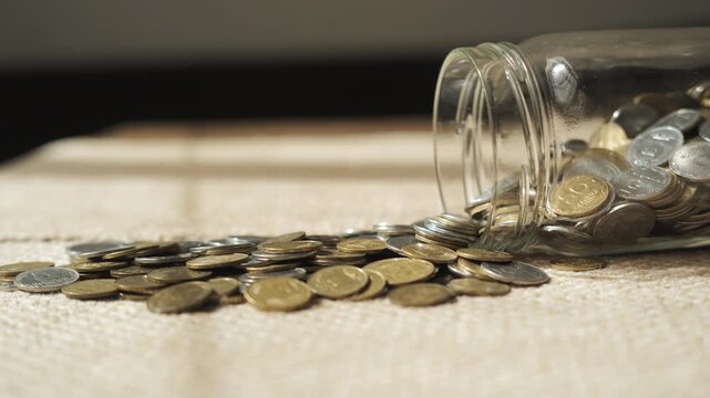 Coins Spilling From Glass Jar Representing Personal Savings Concept, scattered currency illustrating budgeting and financial planning