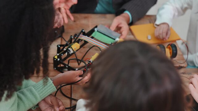 Close up of diverse students and teacher hands building a robot. Teamwork and collaboration during a STEM science project in elementary school.