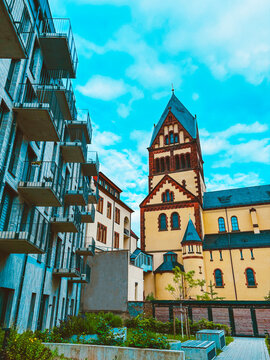 Historic church architecture and modern residential building in urban courtyard under dramatic cloudy blue sky
