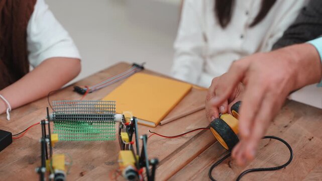 Close up of teacher and student hands pointing at robot wheel. Learning STEM science and engineering project together on wooden desk.