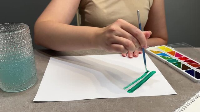 Mid-sequence person painting green watercolor strokes on paper at tabletop workspace under cool