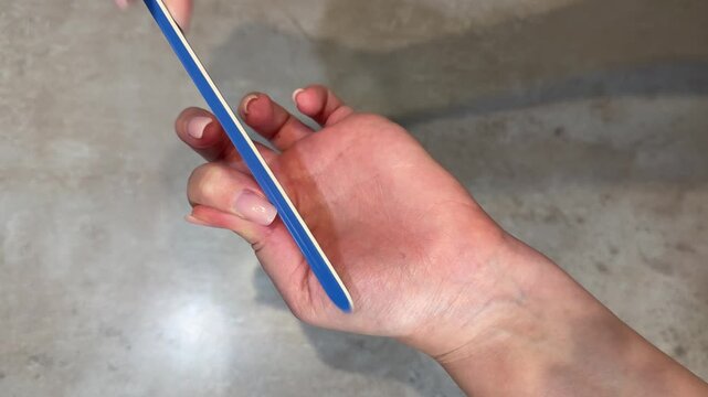 Midsequence closeup of hand manicure filing nails on palm with emery board