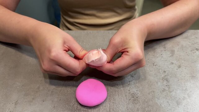 Hands shaping pale pink modeling clay over bright pink disc on concrete countertop mid sequence