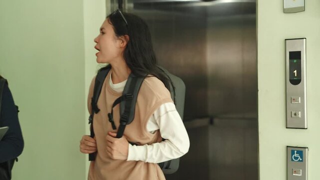 Two smiling diverse women exiting an elevator holding a tablet. Casual students or office colleagues arriving at university or workplace building in the morning.