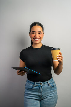 Young woman smiling, holding a digital tablet and takeaway coffee on a light background