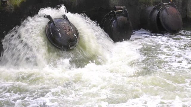 running water violently discharging from large pipe flap valve into river