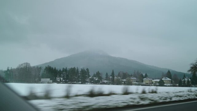 Winter view of snowy hill and frozen lake under cloudy sky in Czech Republic.