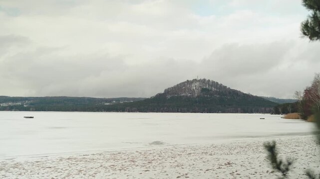 Winter view of snowy hill and frozen lake under cloudy sky in Czech Republic.