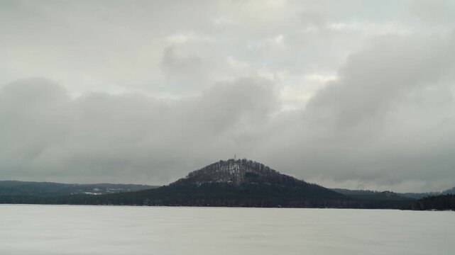Winter view of snowy hill and frozen lake under cloudy sky in Czech Republic.
