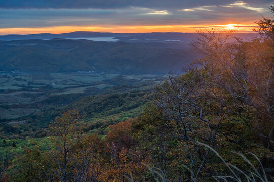 View of the sunrise over rolling hills and mist-covered valleys from Sitno peak in the Stiavnicke vrchy mountains with autumn trees Ilija, Banska Bystrica Region, Slovakia.