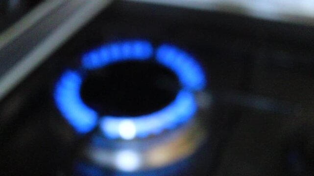 The blue flame of a gas burner on a kitchen stove is out of focus and blurred in slow motion. Close-up of a household gas stove in a dark room, energy consumption during cooking, gas consumption