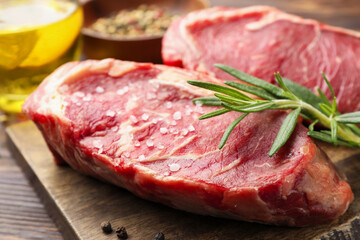 Fototapeta premium Raw beef steaks with salt, rosemary and oil on wooden table, closeup