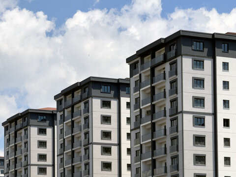 View of modern residential apartment buildings with grey and white facades and glass balconies under a blue sky with clouds in Bagcilar, Istanbul, Turkiye.