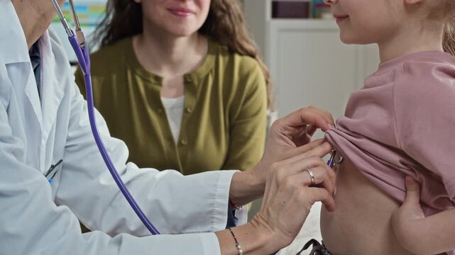 Side view cropped shot of female pediatrician examining young child with stethoscope during medical checkup while mother watching. Perfect for healthcare marketing and pediatric clinic promotions