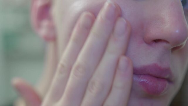 Person applying moisturizing face cream in bathroom mirror. Skincare, beauty routine and personal self care concept.