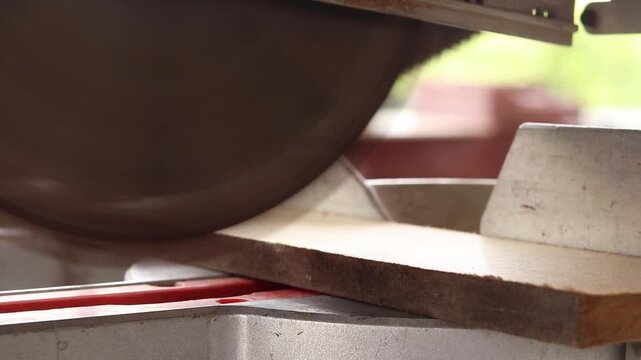 The process of sawing a wooden block with a miter saw. Close-up of the blade in operation. Working with wood, a miter saw cuts a wooden workpiece. The concept of construction and carpentry. Work
