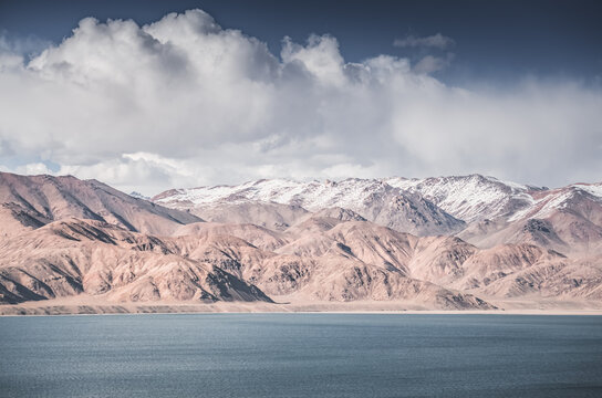 Landscape in the Pamir Mountains with a blue lake Yashilkul in the Tien Shan, a panoramic view of the highlands with snow-capped rocky peaks and the blue waters of the lake
