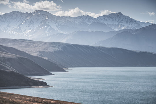 Landscape in the Pamir Mountains with a blue lake Yashilkul in the Tien Shan, a panoramic view of the highlands with snow-capped rocky peaks and the blue waters of the lake