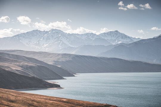 Landscape in the Pamir Mountains with a blue lake Yashilkul in the Tien Shan, a panoramic view of the highlands with snow-capped rocky peaks and the blue waters of the lake