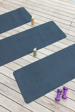 Central slate-blue exercise mat is lying diagonally on wood deck, with bottles and purple weights