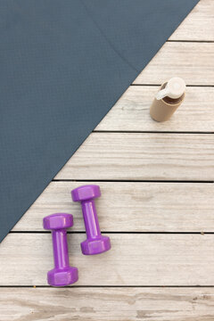 Pair of purple dumbbells are resting on wooden plank floor with charcoal mat and beige bottle