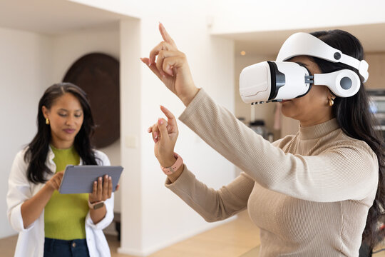 Diverse female coworkers demonstrating virtual reality at home with white headset and tablet