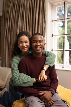 Couple smiling and hugging on living room sofa, woman in green sweater, man in burgundy knit