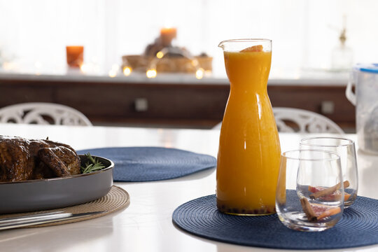Carafe of orange juice and two glasses are sitting on dining table near glazed roast