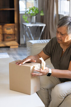 Senior African American woman sitting on sofa pulling packing paper from package on coffee table