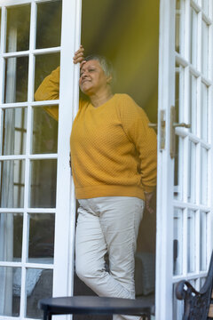 Mature African American woman standing in French door at home wearing yellow sweater touching latch