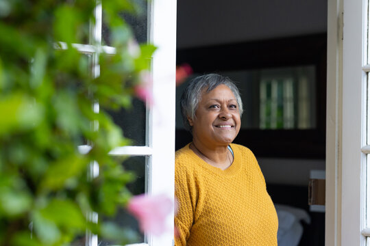 Senior African woman standing in white door frame smiling wearing mustard sweater with pink flowers
