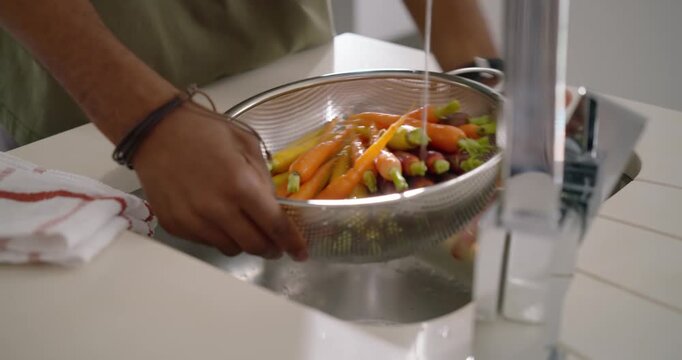 Diverse couple rinsing multicolor carrots under running faucet while woman snipping chives for meal