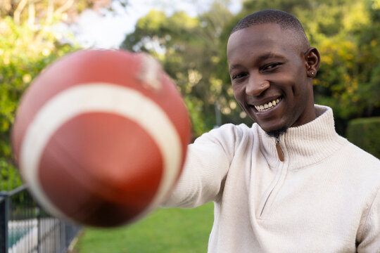 African American man holding football on lawn, smiling, zip sweater, nose stud showing, copy space