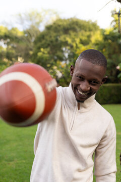 Adult man leaning and holding blurred football near camera on lawn in quarter-zip, studs, nose ring