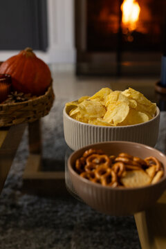 White ribbed ceramic bowl of potato chips is reflecting on glass table, with fireplace glowing