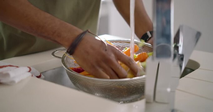 Diverse duo starting faucet rinsing carrots in colander while snipping herbs with scissors for meal