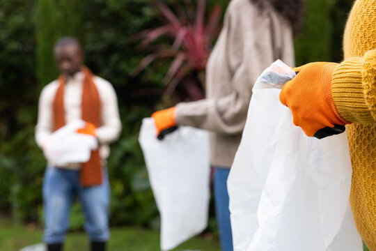 African American volunteers in orange-gloves yellow-sweater picking white-bags in park, copy space