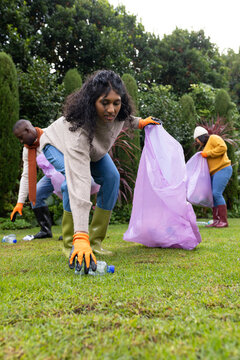 African American volunteers collecting litter on lawn in garden with lavender bags and bottles