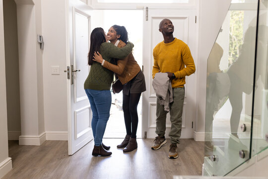 African American friends hugging in residential foyer by open front door, man holding light jacket