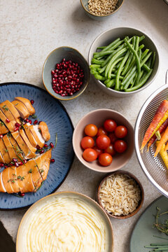 Sliced roasted poultry breast is resting on blue plate, on beige stone counter with colorful bowls